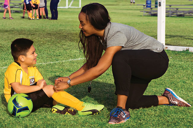 Woman tying child's shoe on a soccer field