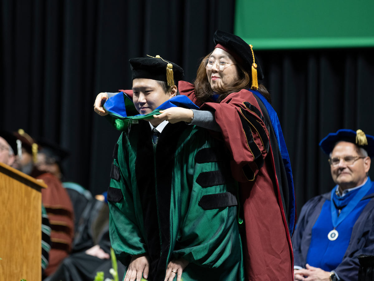 Graduate student being hooded on stage at commencement
